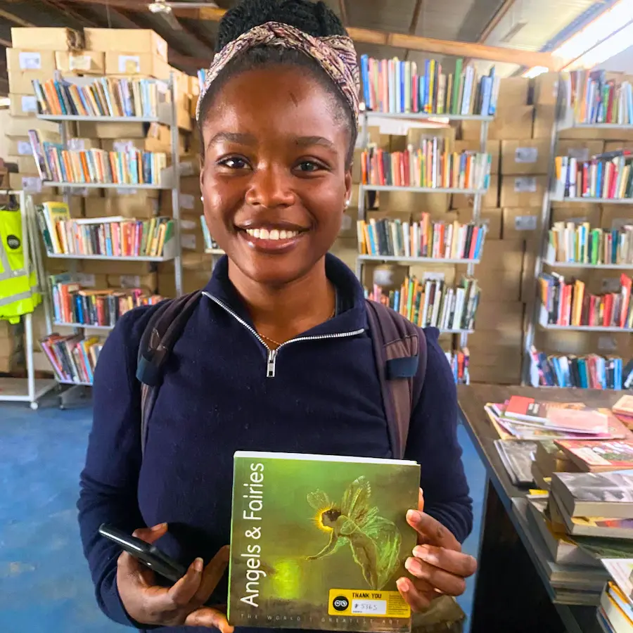 Smiling young woman holding a donated book in front of shelves of books